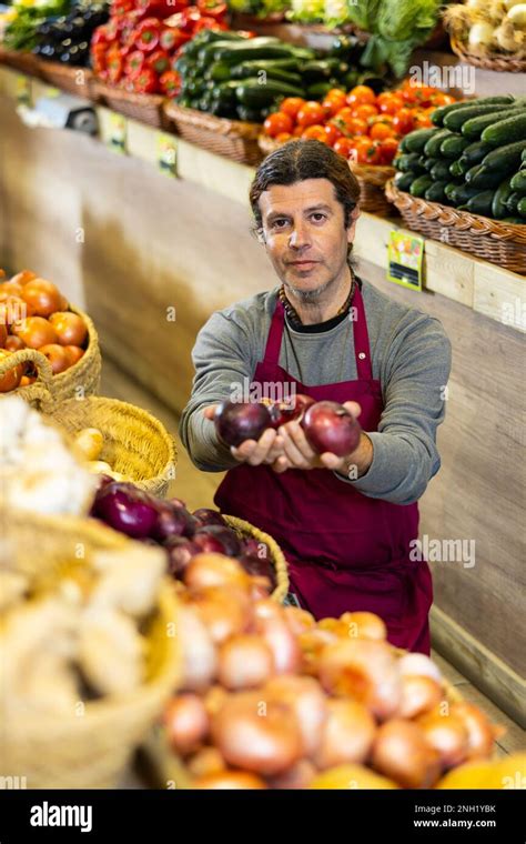 Male Grocery Store Worker Arranges Red Onion And Other Vegetables On